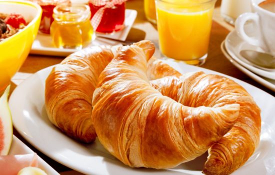 Delicious continental breakfast with fresh flaky croissants, assorted preserves, orange juice , cereal and coffee, close up on the croissants